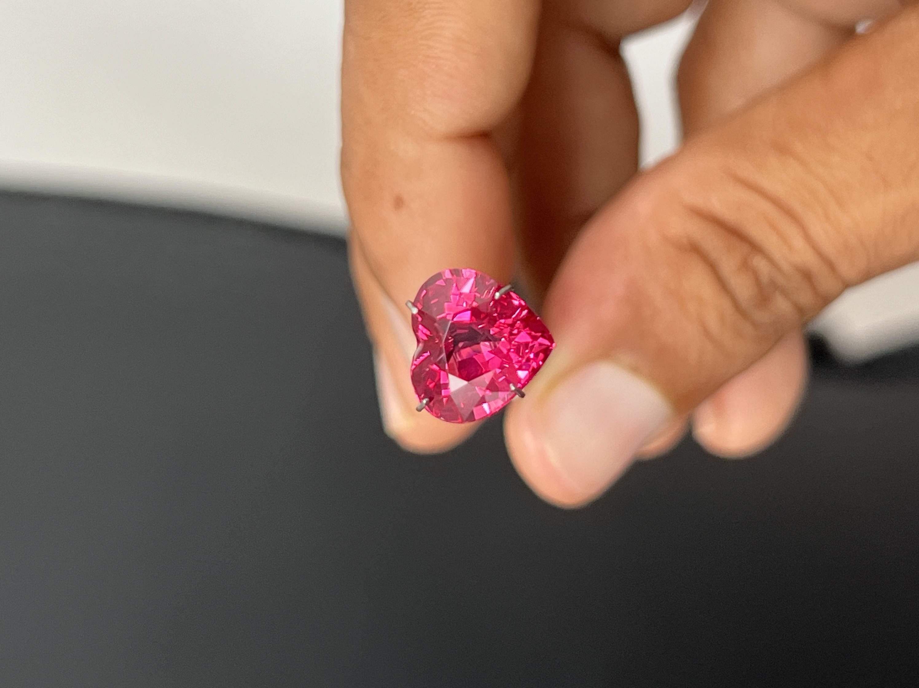 A finished pink heart-shaped gemstone held face-up in a hand, with the complete outline visible.
