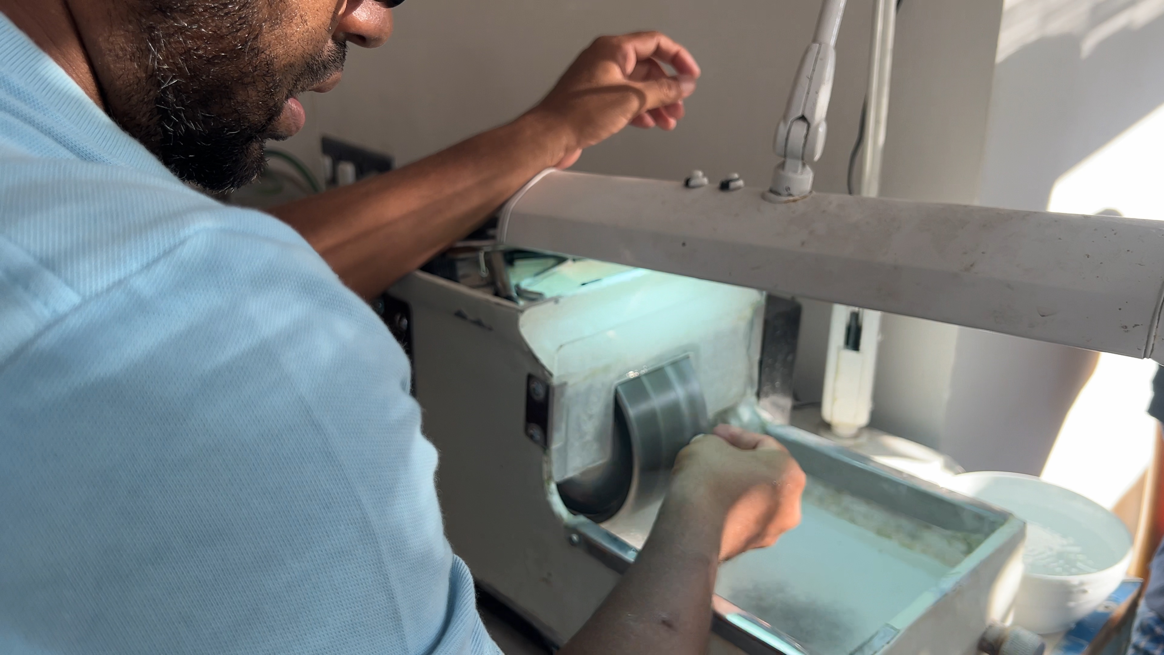 A person works at a lapidary wheel, holding material at the working surface.